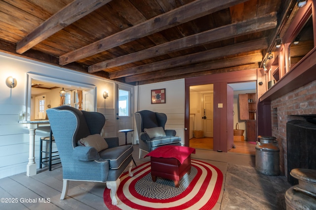 living area featuring beamed ceiling, wood walls, a brick fireplace, and wood ceiling