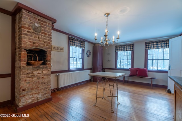 dining area featuring ornamental molding, hardwood / wood-style floors, radiator, a fireplace, and a chandelier