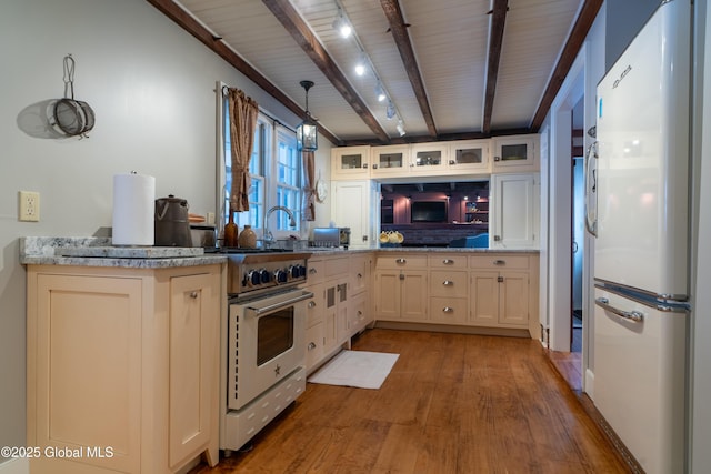 kitchen featuring wood finished floors, beam ceiling, freestanding refrigerator, stainless steel range, and glass insert cabinets