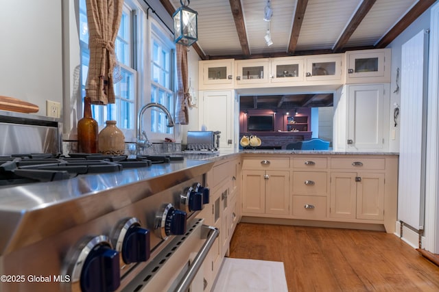 kitchen with glass insert cabinets, beamed ceiling, light wood-style floors, and light stone countertops