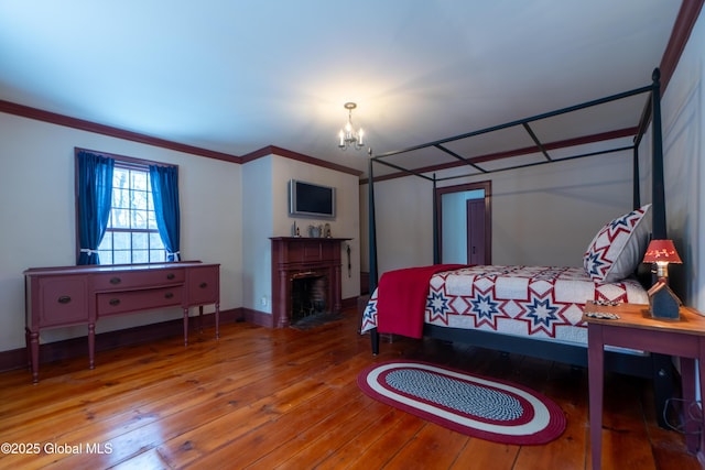 bedroom with a fireplace with flush hearth, ornamental molding, hardwood / wood-style flooring, an inviting chandelier, and baseboards