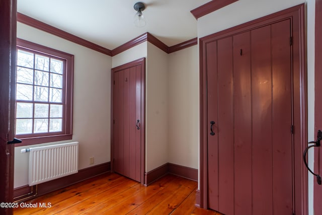 unfurnished bedroom featuring light wood finished floors, baseboards, radiator heating unit, ornamental molding, and a closet