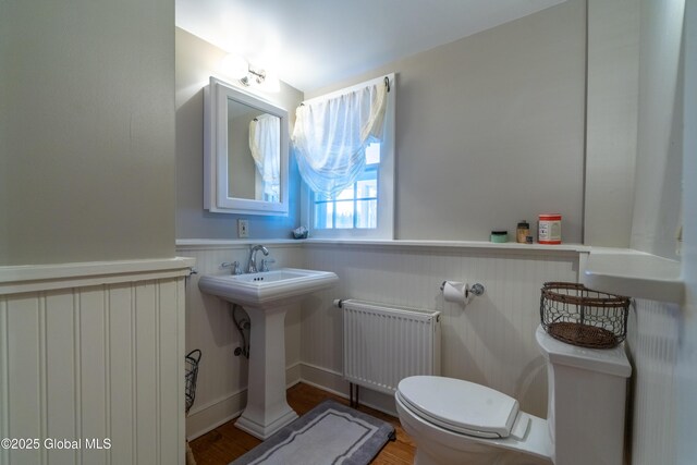 bathroom with wood finished floors, toilet, wainscoting, and radiator heating unit