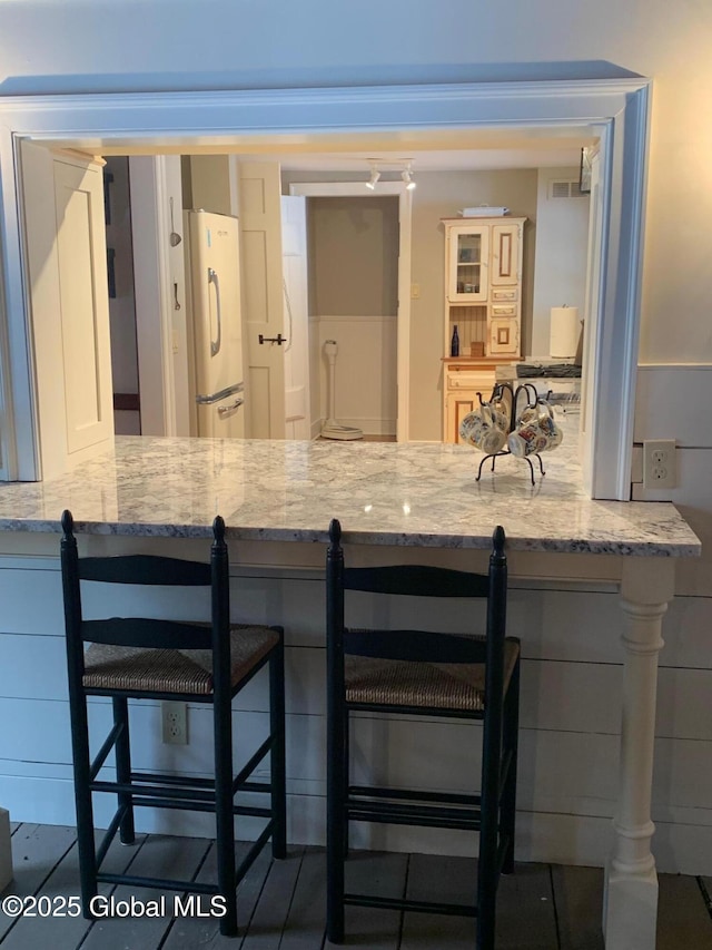 interior space with light stone counters, a breakfast bar, and freestanding refrigerator