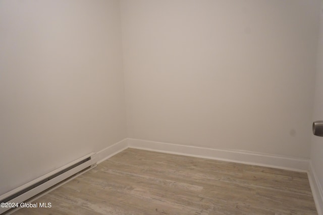 unfurnished room featuring a baseboard heating unit, baseboards, and wood finished floors