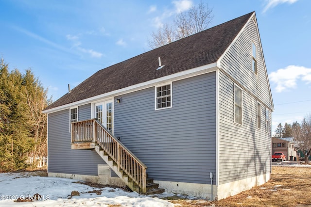 snow covered property featuring stairway and roof with shingles