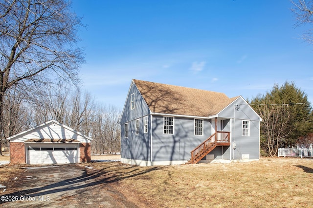 view of front of house featuring a shingled roof, a detached garage, a front lawn, and an outbuilding