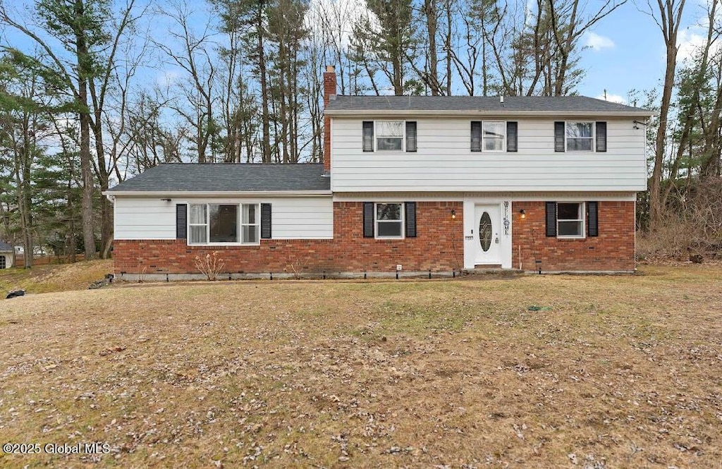 colonial house with a front lawn, a chimney, and brick siding