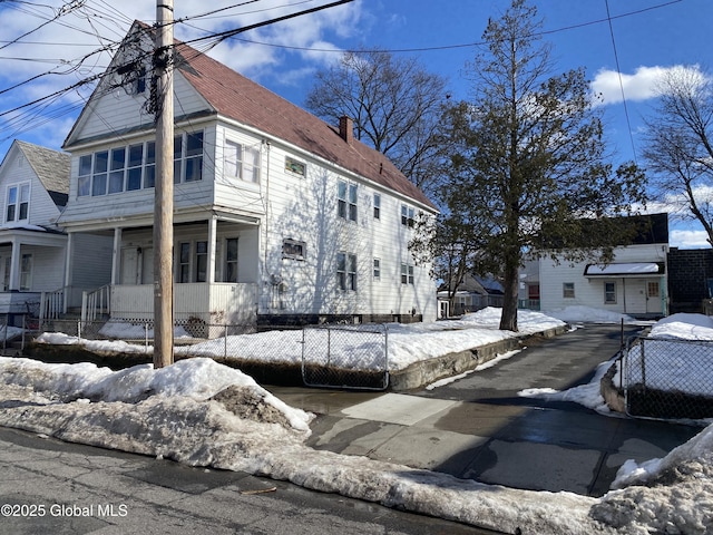 view of snow covered exterior with a chimney, fence, and a porch