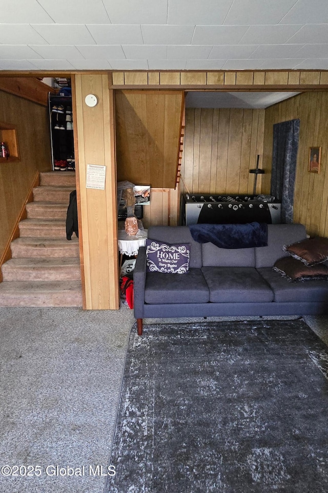 living room with carpet floors, wood walls, and stairs