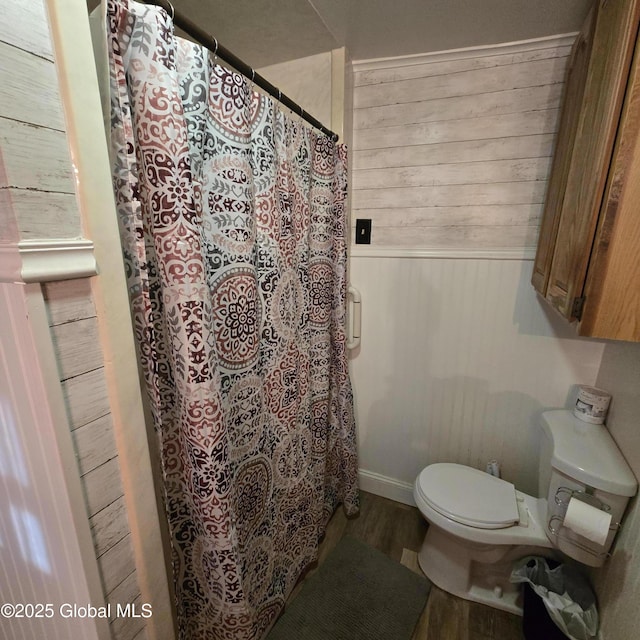 bathroom with a shower with shower curtain, wood finished floors, toilet, and wooden walls