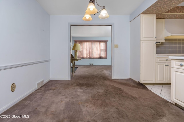 unfurnished dining area with carpet, visible vents, baseboards, and an inviting chandelier