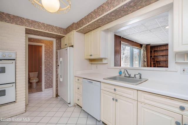 kitchen featuring light countertops, white cabinetry, a sink, white appliances, and wallpapered walls