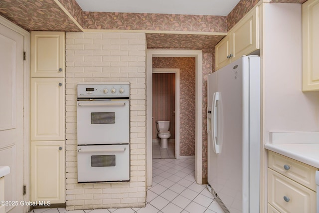 kitchen featuring light tile patterned floors, white appliances, cream cabinetry, and wallpapered walls