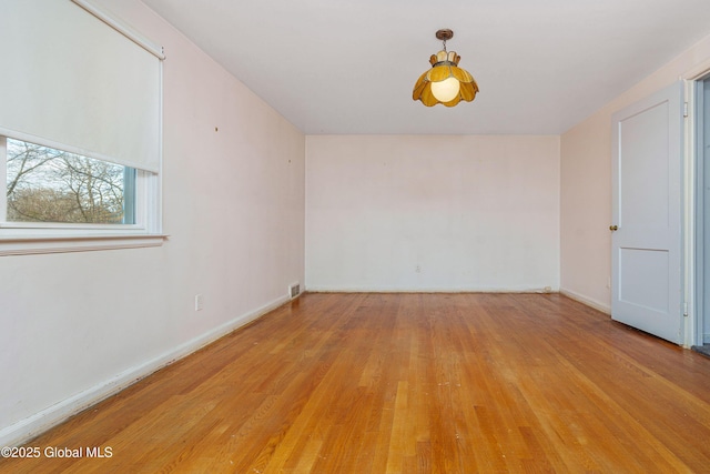 empty room with light wood finished floors, visible vents, and baseboards