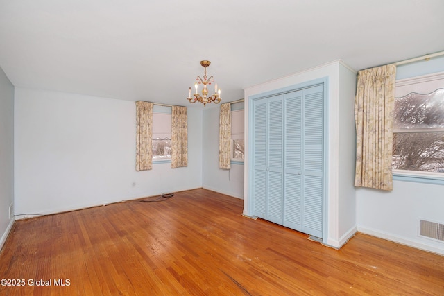 unfurnished bedroom featuring a closet, visible vents, wood finished floors, a chandelier, and baseboards