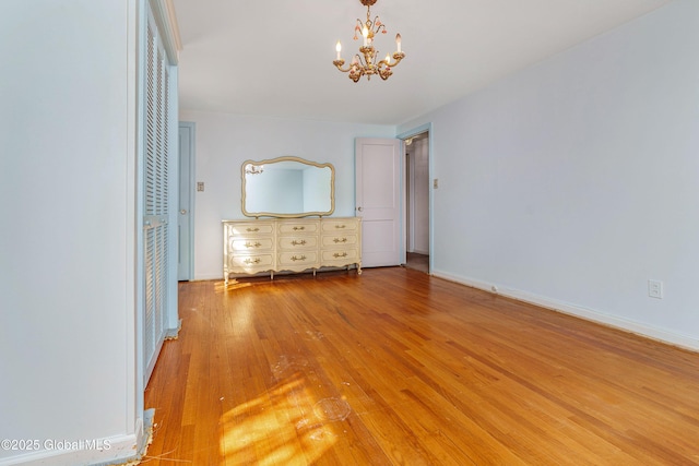 unfurnished bedroom featuring baseboards, wood finished floors, and an inviting chandelier