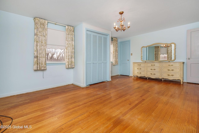 unfurnished bedroom featuring a chandelier, a closet, wood finished floors, and baseboards