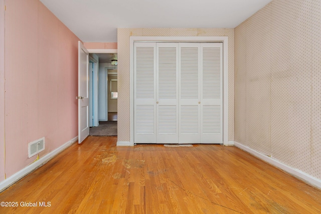 unfurnished bedroom with a closet, visible vents, light wood-style flooring, baseboards, and wallpapered walls