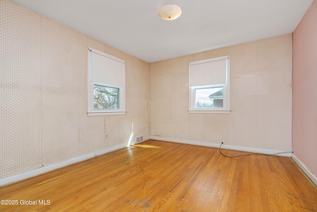 unfurnished room featuring a wealth of natural light, light wood-type flooring, visible vents, and wallpapered walls