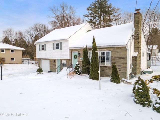 tri-level home featuring an attached garage, stone siding, and a chimney