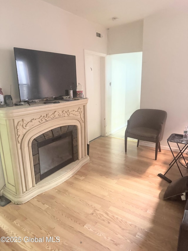 living area with light wood-style flooring, a fireplace, visible vents, and baseboards