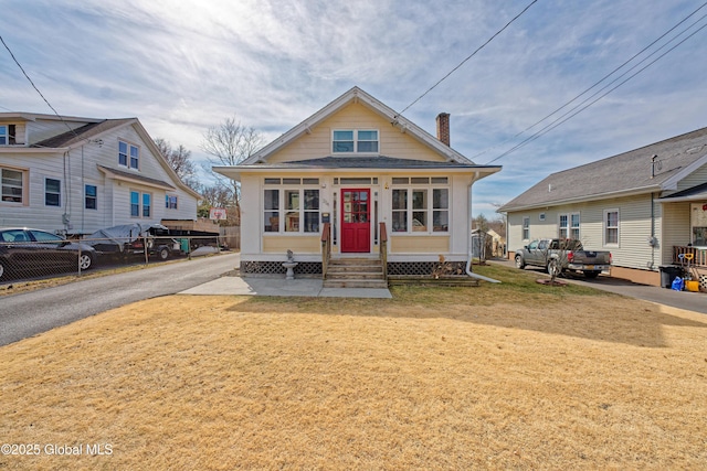 view of front of property featuring entry steps, a front lawn, fence, and a chimney