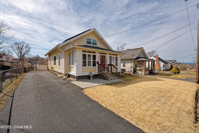 bungalow-style house with aphalt driveway, fence, and a front lawn