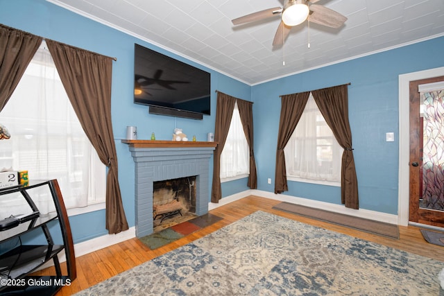 living area featuring wood finished floors, a brick fireplace, ceiling fan, and ornamental molding