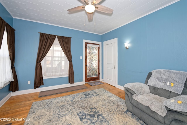 living area featuring baseboards, wood finished floors, ceiling fan, and ornamental molding