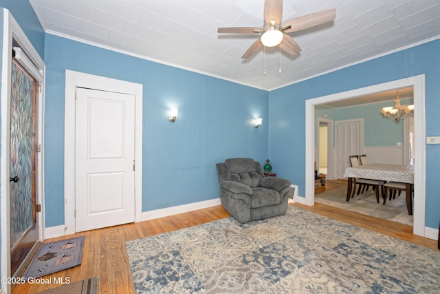 living area featuring ceiling fan with notable chandelier, wood finished floors, baseboards, and ornamental molding