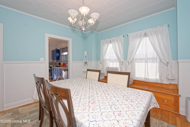 dining space featuring wainscoting, crown molding, an inviting chandelier, and wood finished floors