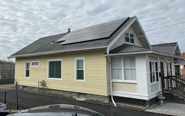 view of property exterior with fence, solar panels, and a shingled roof