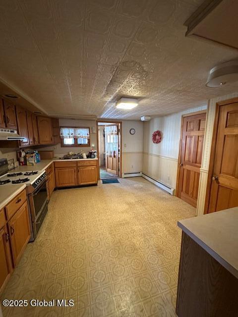 kitchen featuring brown cabinetry, gas range oven, under cabinet range hood, and light countertops