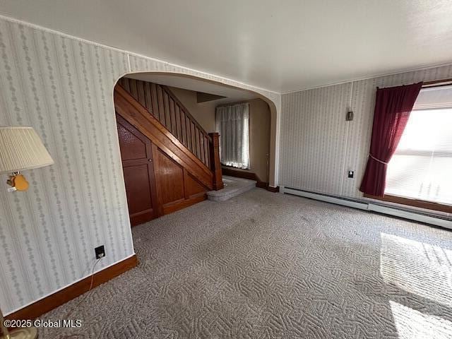 spare room with stairway, wallpapered walls, arched walkways, a baseboard heating unit, and light colored carpet