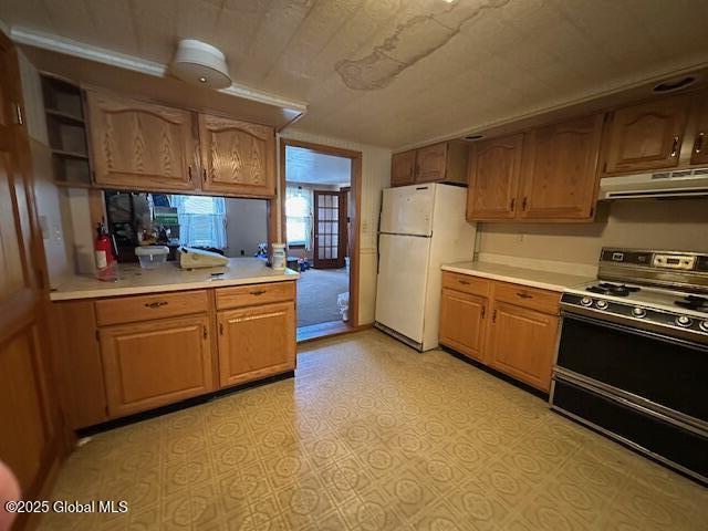 kitchen featuring under cabinet range hood, light floors, light countertops, gas range oven, and freestanding refrigerator