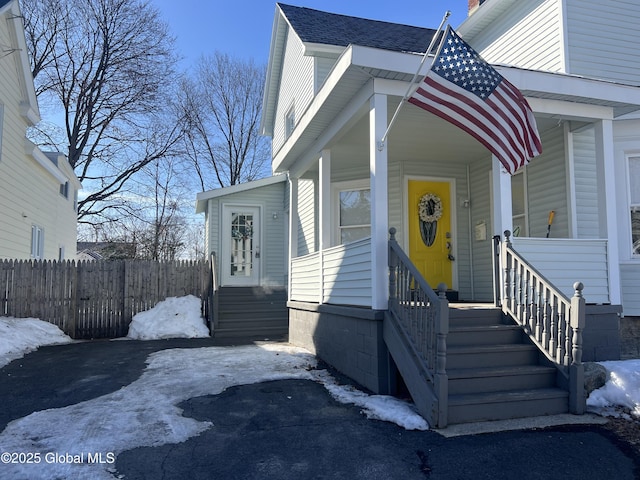 view of front of home with entry steps, a porch, roof with shingles, and fence