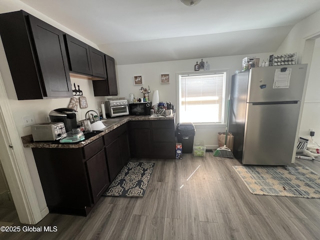 kitchen featuring a toaster, a sink, wood finished floors, vaulted ceiling, and freestanding refrigerator