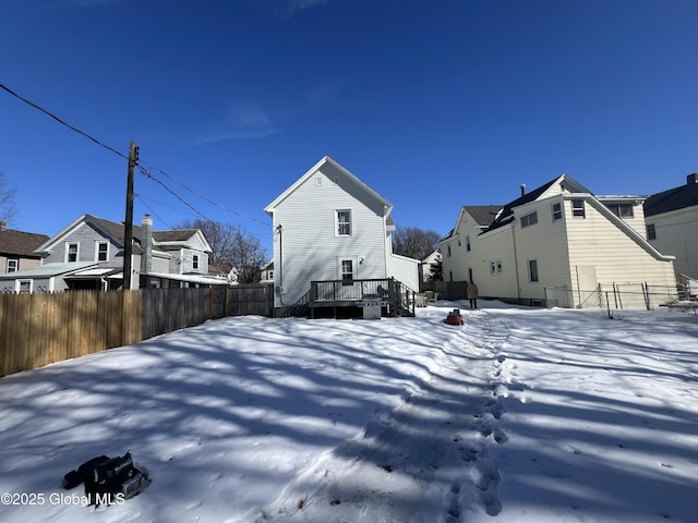 snow covered rear of property featuring a deck, a fenced backyard, and a residential view