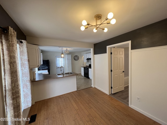 kitchen featuring hardwood / wood-style floors, a peninsula, a sink, black appliances, and a notable chandelier