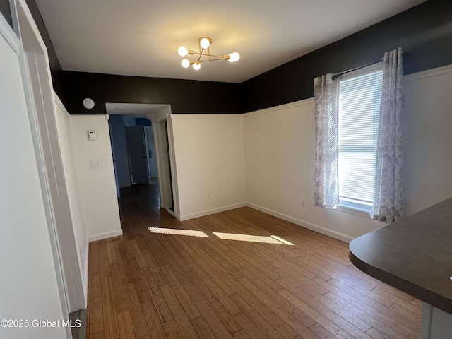 unfurnished dining area with an inviting chandelier, wood-type flooring, and baseboards