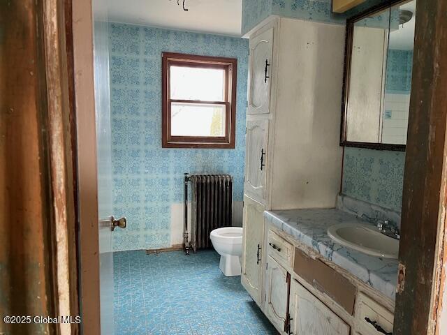 bathroom with toilet, vanity, radiator heating unit, and wallpapered walls