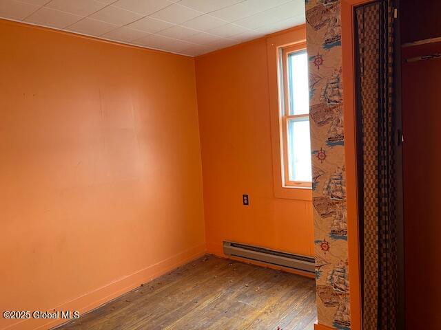 unfurnished room featuring wood-type flooring and a baseboard heating unit