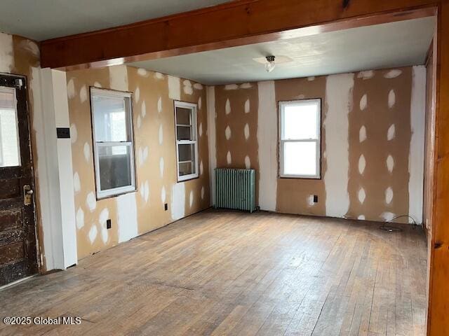 unfurnished room with beamed ceiling, radiator heating unit, and hardwood / wood-style flooring