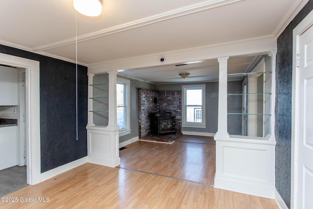 interior space with a wood stove, ornate columns, crown molding, and wood finished floors