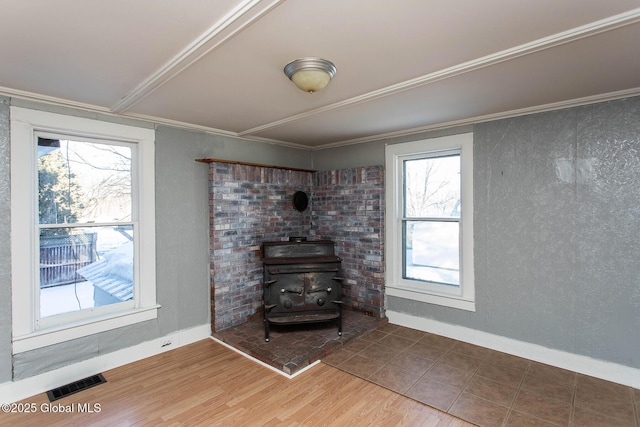 unfurnished living room with a wood stove, visible vents, wood finished floors, and ornamental molding