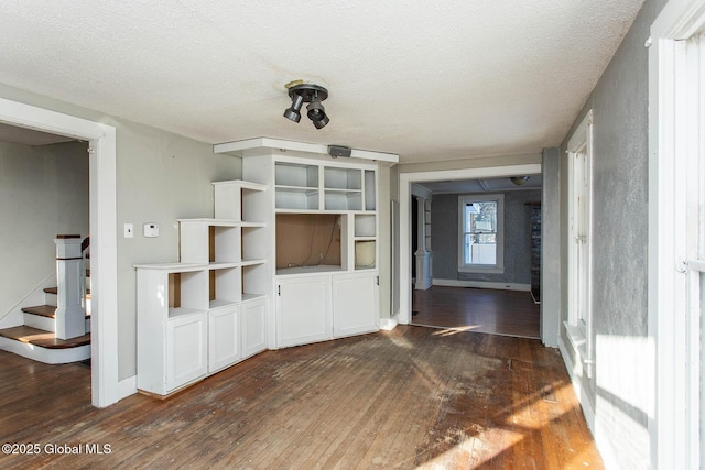 unfurnished living room featuring a textured ceiling, stairs, baseboards, and dark wood-type flooring