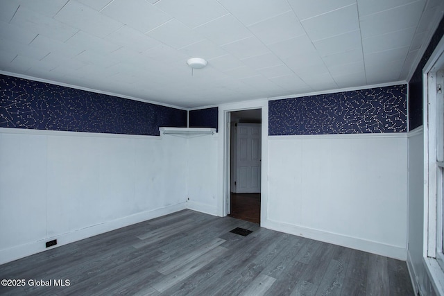 unfurnished room featuring a wainscoted wall, wood finished floors, visible vents, wallpapered walls, and crown molding