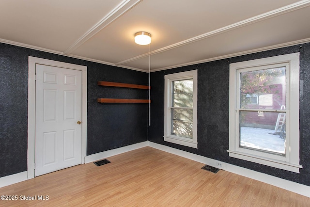 unfurnished room featuring light wood-type flooring, plenty of natural light, visible vents, and crown molding