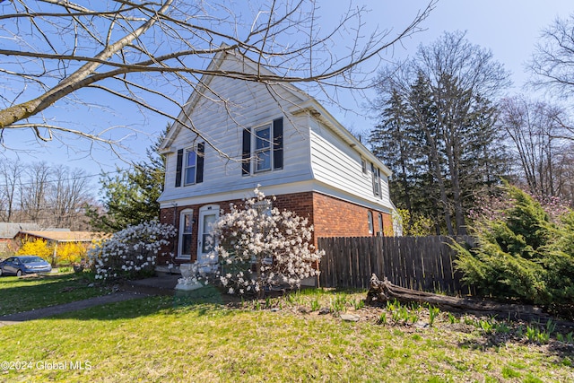 view of property exterior featuring brick siding, fence, and a lawn